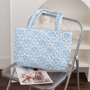 Detailed texture of blue floral quilted tote bag resting on a transparent chair