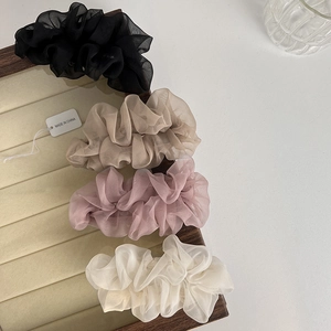 Detail of four organza hair scrunchies in black, beige, pink, and white on a wooden tray
