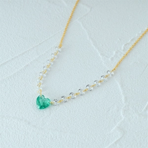 Close-up of golden necklace featuring a green heart-shaped pendant with crystal accents