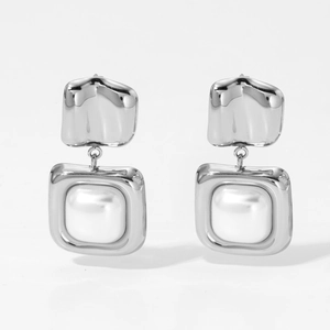 Macro view of geometric stainless steel square pendant earrings with white pearl detail