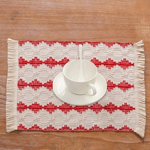 Detail of cream and red woven place mat with tassels on a wooden table setup