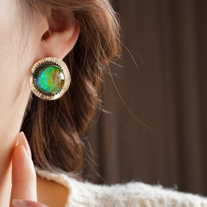 Close-up of vintage golden round earrings with iridescent resin gemstone on model