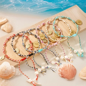 Handmade Peruvian cotton cord bracelet with gold coin charms and pearls on a beach setting