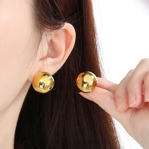 Close-up of a model wearing polished golden ball stud earrings made of titanium steel