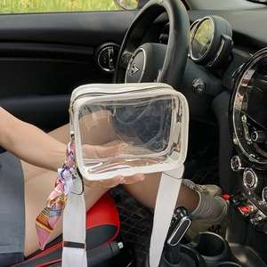Transparent crossbody bag with white leather trim and silk scarf on car interior background