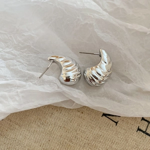 Close-up of silver conch-shaped stud earrings with spiral texture on linen background