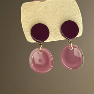 Close-up of irregular purple and translucent pink resin drop earrings with gold links