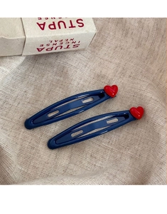 Detail of two navy blue heart hair clips with red accents on a soft linen background