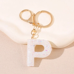 Gros plan du porte-clés doré lettre P en résine pailletée blanche sur socle beige