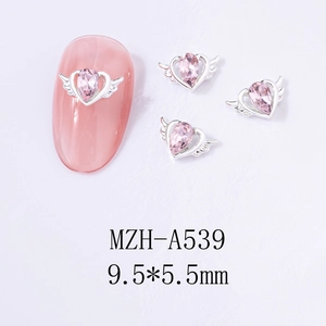 Macro detail of winged heart nail charms with pink pear-cut gemstones and alloy finish
