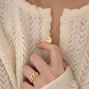 Golden minimalist oval pendant necklace and woven chain ring styled on a white sweater