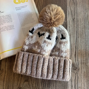 Close-up of thick knit beanie featuring a brown faux fur pompom on a wooden background