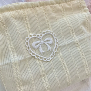 Detail of cream fabric pouch with white lace heart patch and bow embroidery