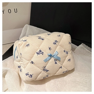 Quilted beige cosmetic bag with blue floral patterns and a small decorative bow