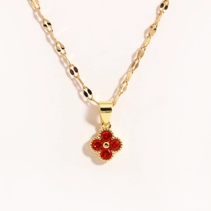 Dettaglio di una collana dorata con ciondolo a quadrifoglio rosso e intarsio di rubini
