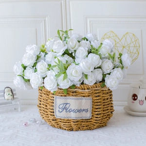 Detail of white artificial silk roses arranged in a woven grass basket with Flowers label