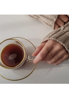 Close-up of minimalist gold thin rings worn with a cozy knit sweater and coffee
