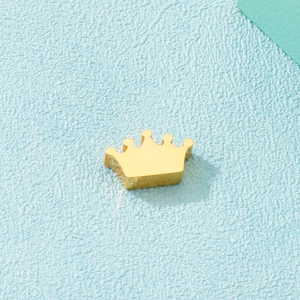 Macro shot of a minimalist gold stainless steel crown pendant on a light blue background
