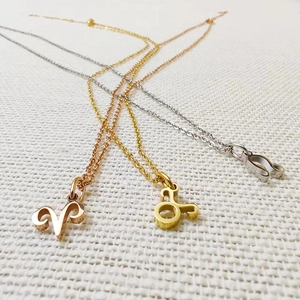 Detailed view of Zodiac pendants in rose gold, gold, and silver on white knit fabric
