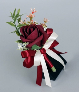 Détail d'une boutonnière de rose rouge avec rubans en soie et petites feuilles vertes