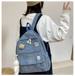 Detalle de mochila de pana azul claro con insignias de osos y colgante de peluche