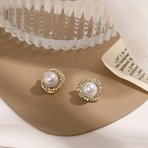 Detail of elegant gold earrings with center white pearl and sparkling rhinestone halo
