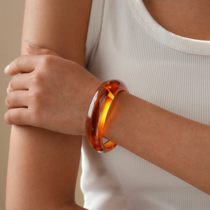 Close-up of translucent amber resin geometric open bangle on model wearing white
