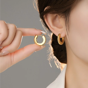 Close-up of a model wearing a small polished gold hoop earring with a minimalist finish