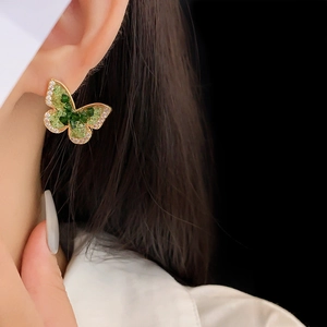 Detailed view of a gold-plated butterfly earring with green crystals and zircon inlays