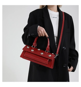 Detail of red glossy leather baguette bag with silver studs worn by a model