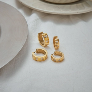 Detailed view of gold hoop earrings with zircon heart and star patterns on fabric