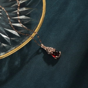 Rose gold PiXiu necklace with red gemstone pendant on textured glass and green fabric