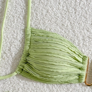 Detail of light green bikini fabric with textured pleats and a gold metal ring link