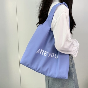 Close-up of a lilac canvas tote bag with white text held by a model in casual outfit
