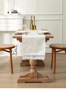 Detail of white jacquard table runner with leaf patterns and elegant woven tassels