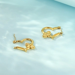 Macro view of gold heart hoop earrings with 3D bee charms on a blue wavy surface