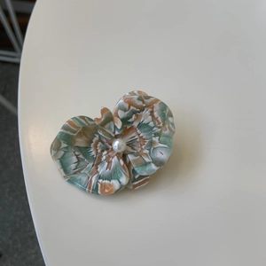 Macro view of floral acetate hair clip with green-orange texture and a center pearl