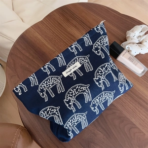 Detail view of navy blue canvas makeup bag with white animal patterns on wooden desk