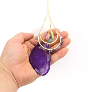 Detail of hanging purple agate slice pendant with gold chains and colorful crystal teardrop