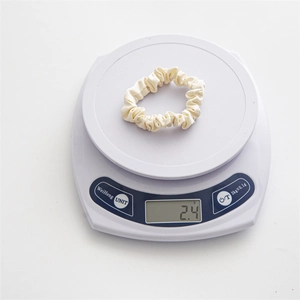Detail view of a cream satin scrunchie on a digital scale showing light 2.4g weight