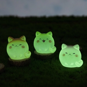 Three cute luminous cat resin figurines glowing in green light on wooden base