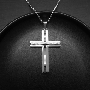 Polished silver cross pendant on box chain displayed on a sleek black ceramic tray