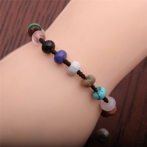 Macro detail of hand-woven bracelet with colorful natural stones on a dark wood background