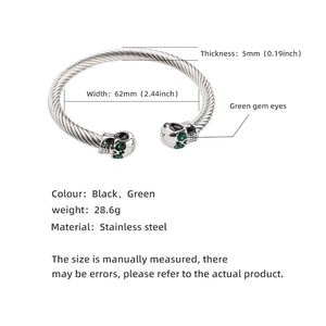 Detail view of C-shaped stainless steel skull bangle with green eyes and twisted wire design
