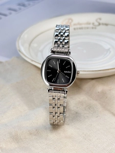 Close-up of a silver square-dial watch with black face on light fabric background