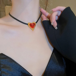 Detail of red resin heart pendant with textured gold border on a black choker