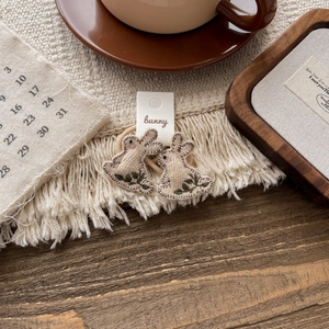 Detailed view of beige embroidered bunny hair ties on white paper card packaging