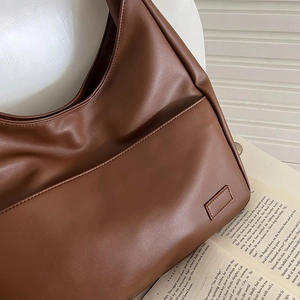 Detail einer braunen Leder-Schultertasche mit Fronttasche auf einem offenen Buch