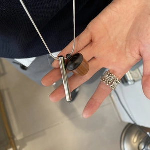 Detail of wooden acorn pendant with silver metal cylinder on a sleek snake chain