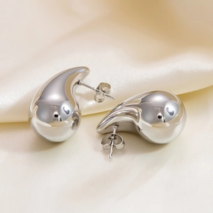 Close-up of silver hollow teardrop earrings on elegant beige silk fabric background